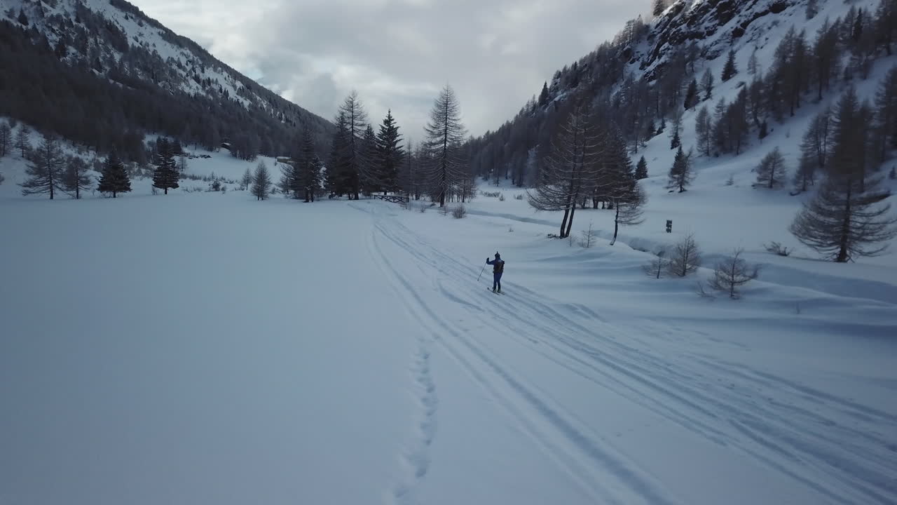 Ripresa aerea con drone di uno sciatore professionista solitario che scia lungo un sentiero montuoso innevato