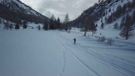 Aerial-drone-shot-of-lone-professional-skier-skiing-through-snowy-mountainous-trail