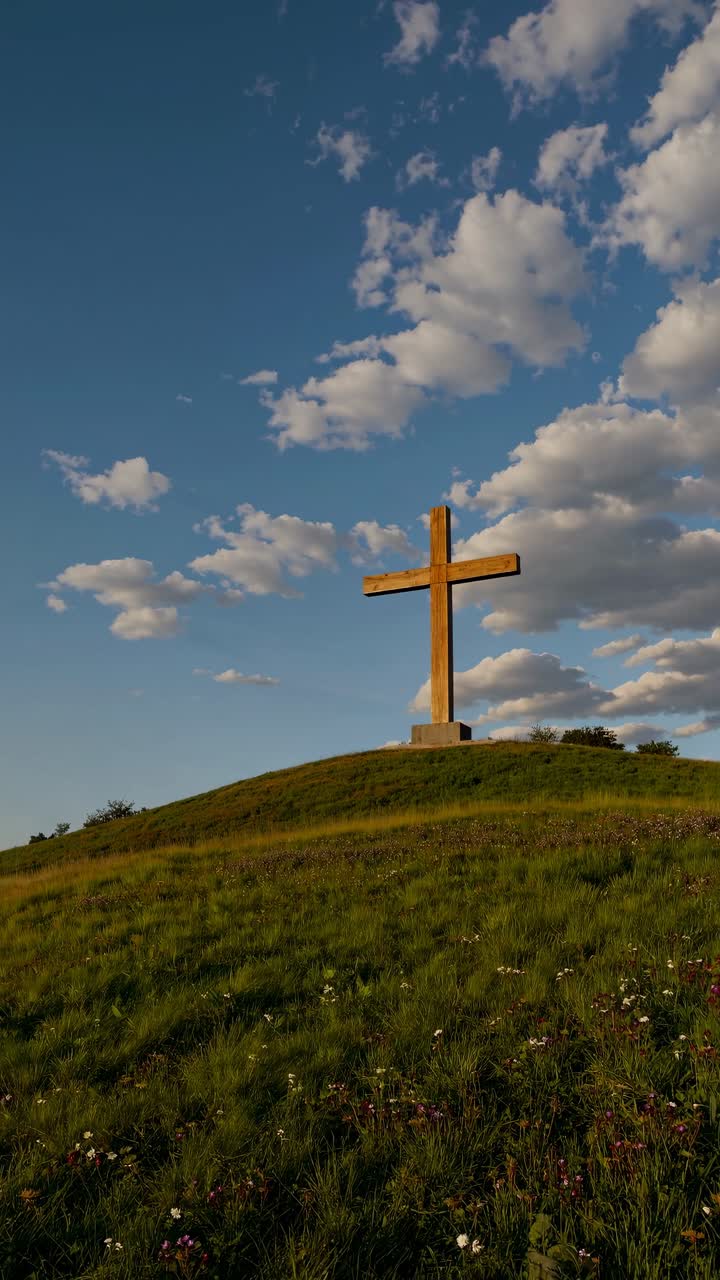 Low-angle shot of a wooden cross on a grassy hill under a blue sky with clouds, evoking a serene