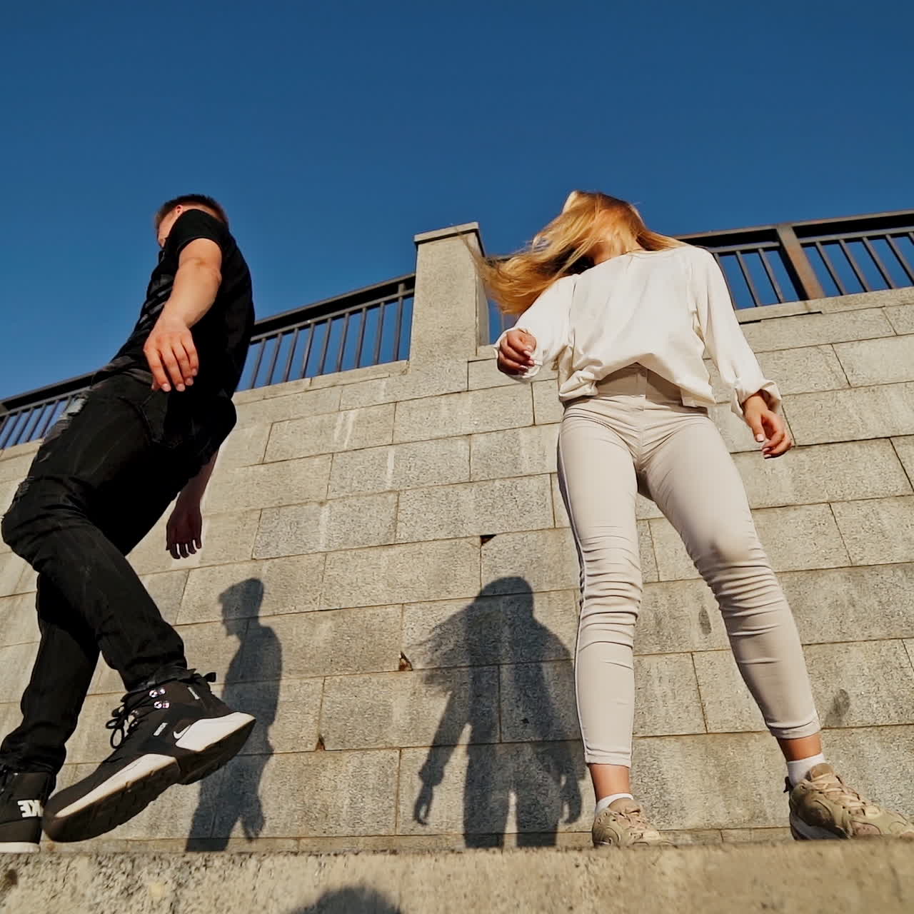 Happy teens near the wall. Young man in black and woman in white outdoors. Slow motion. View from below.