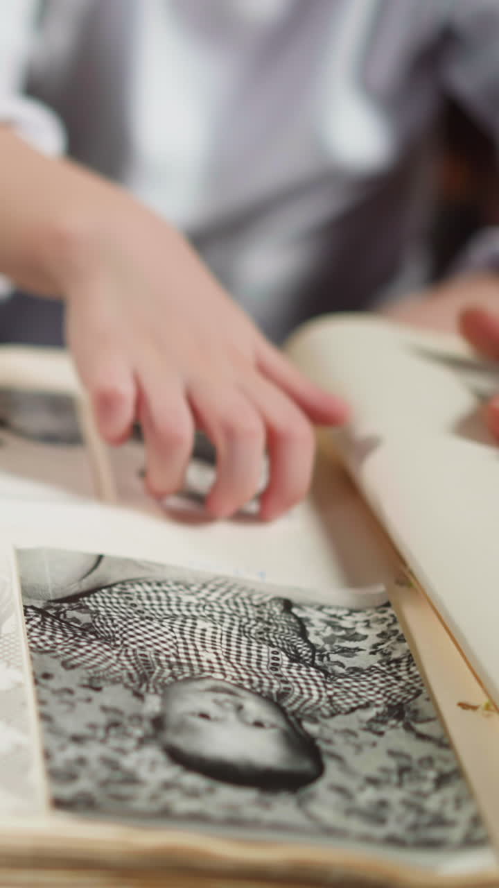Little girl scratches picture of baby grandfather looking at old family photo album with African-American step-father at home closeup slow motion