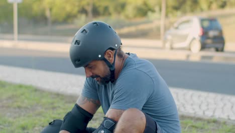 mid adult skateboarder sitting on street tying shoelaces