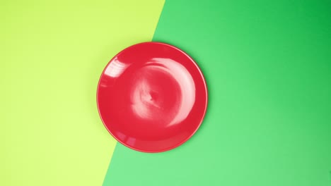 female hand puts on green surface an empty round red ceramic plate