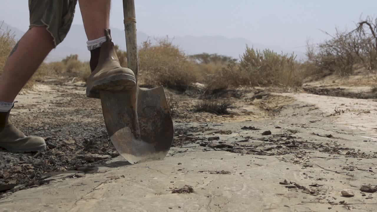 Low POV of man with shovel cleaning up desert area with oil spill