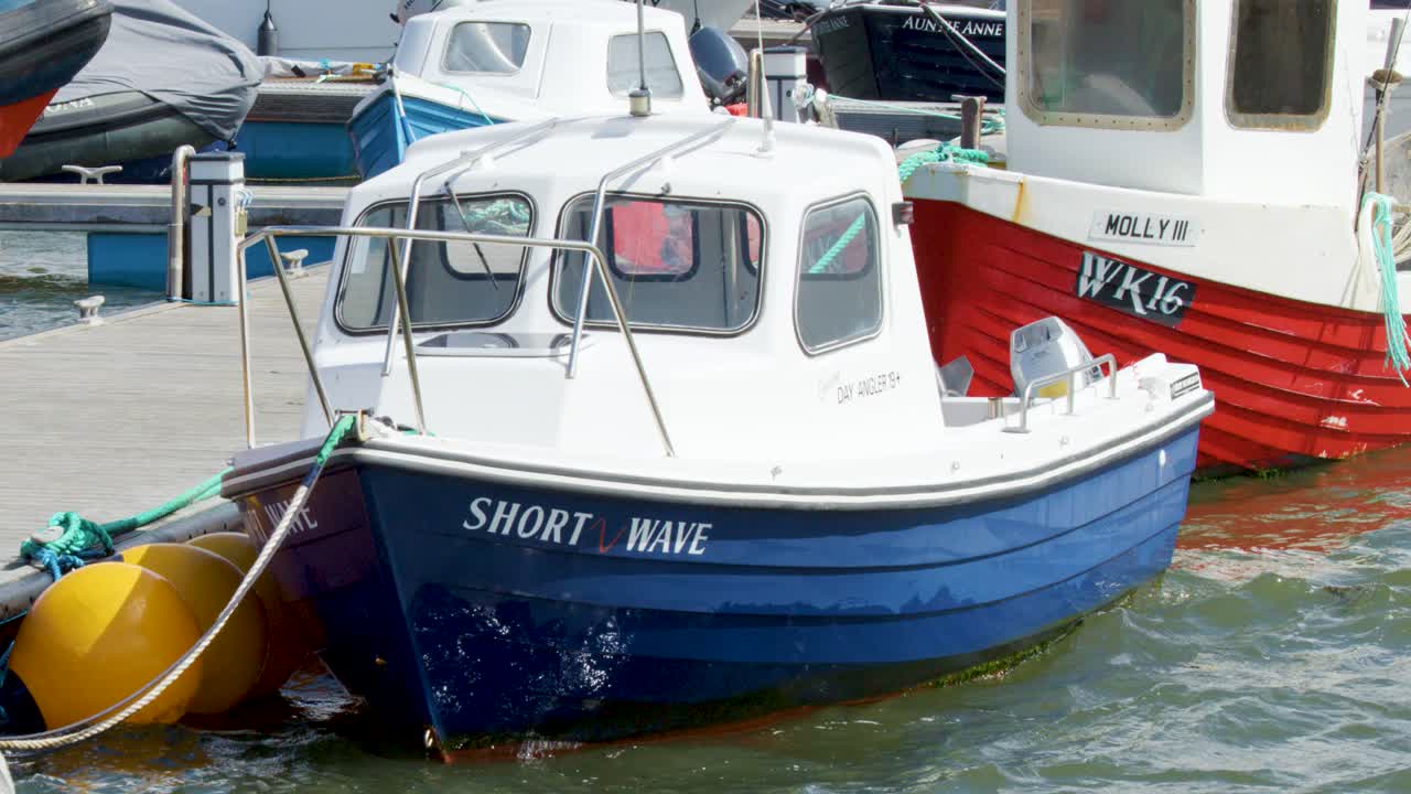 Two small fishing boats gently rock in a busy Cromarty harbour under daylight, with visible movement from rough water and moored buoys