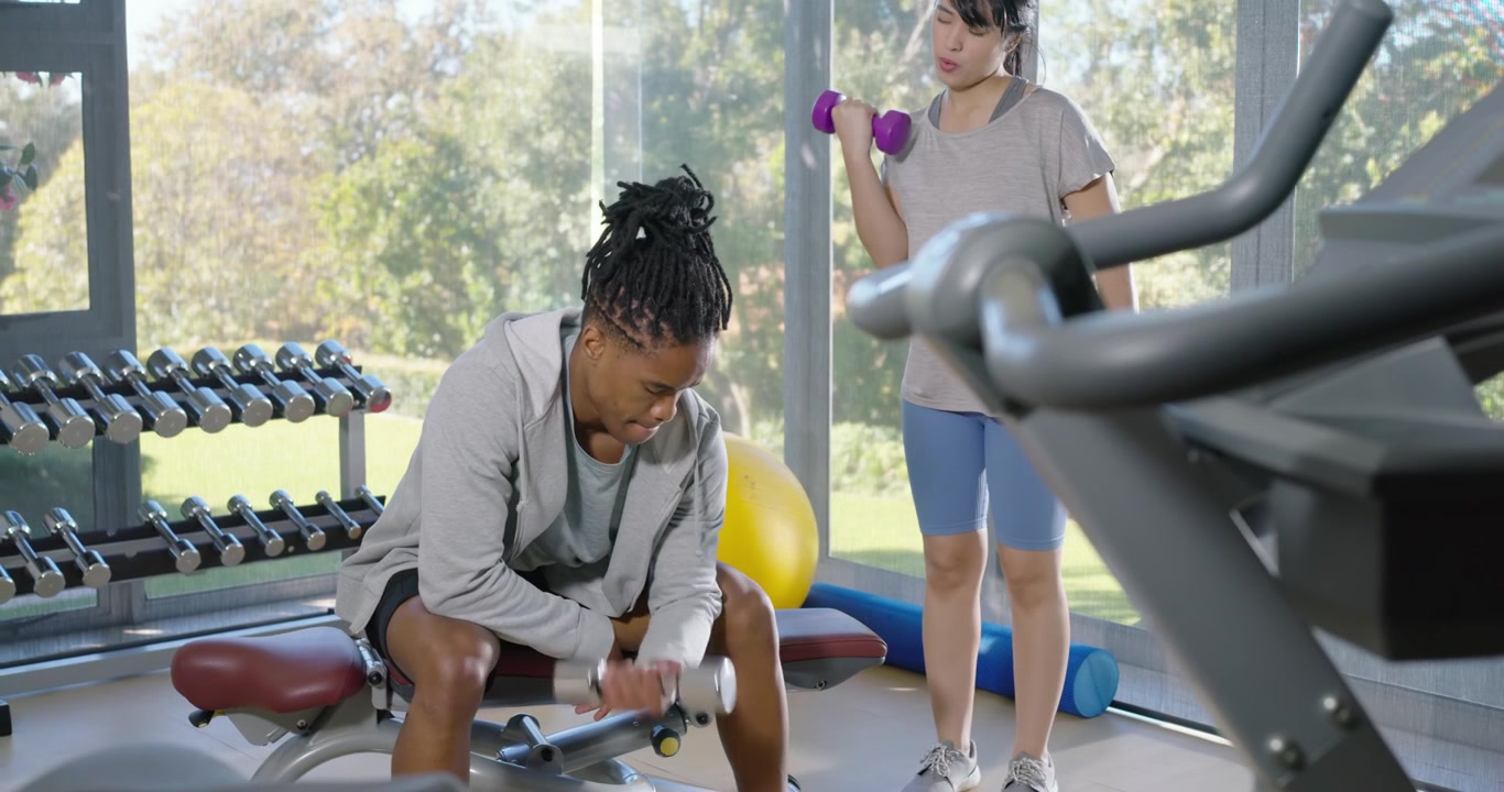 African American pair starting man lifting dumbbell in gym, woman curling weights, training biceps