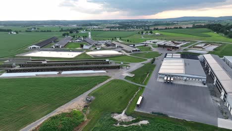 expansive aerial shot capturing an industrial farm, with multiple sheds, storage facilities, and vast surrounding green fields, under a cloudy sky in usa