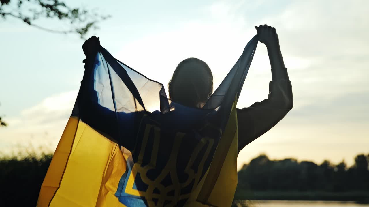 Trefork-våpenskjoldet gløder i solnedgangslyset mens en kvinne vifter med det ukrainske flagget med håp.
