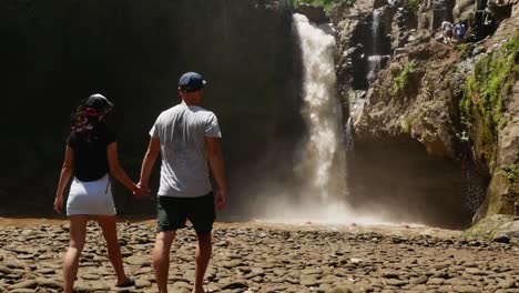 la pareja que viene a la hermosa cascada y levanta la mano