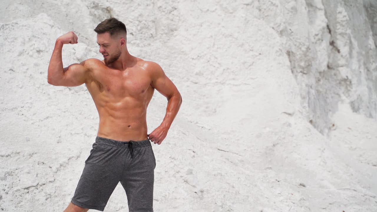 Portrait of handsome bodybuilder outdoors. Strong man shows his trained body with strong muscles while standing in white canyon.