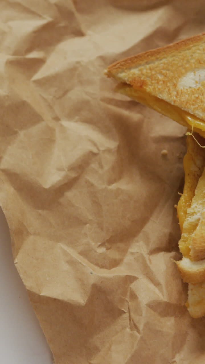 Video of close up of toasted cheese sandwiches on brown paper over grey background