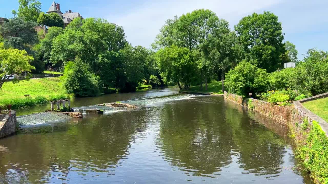 Beautiful reflections of green deciduous trees in river with weir.