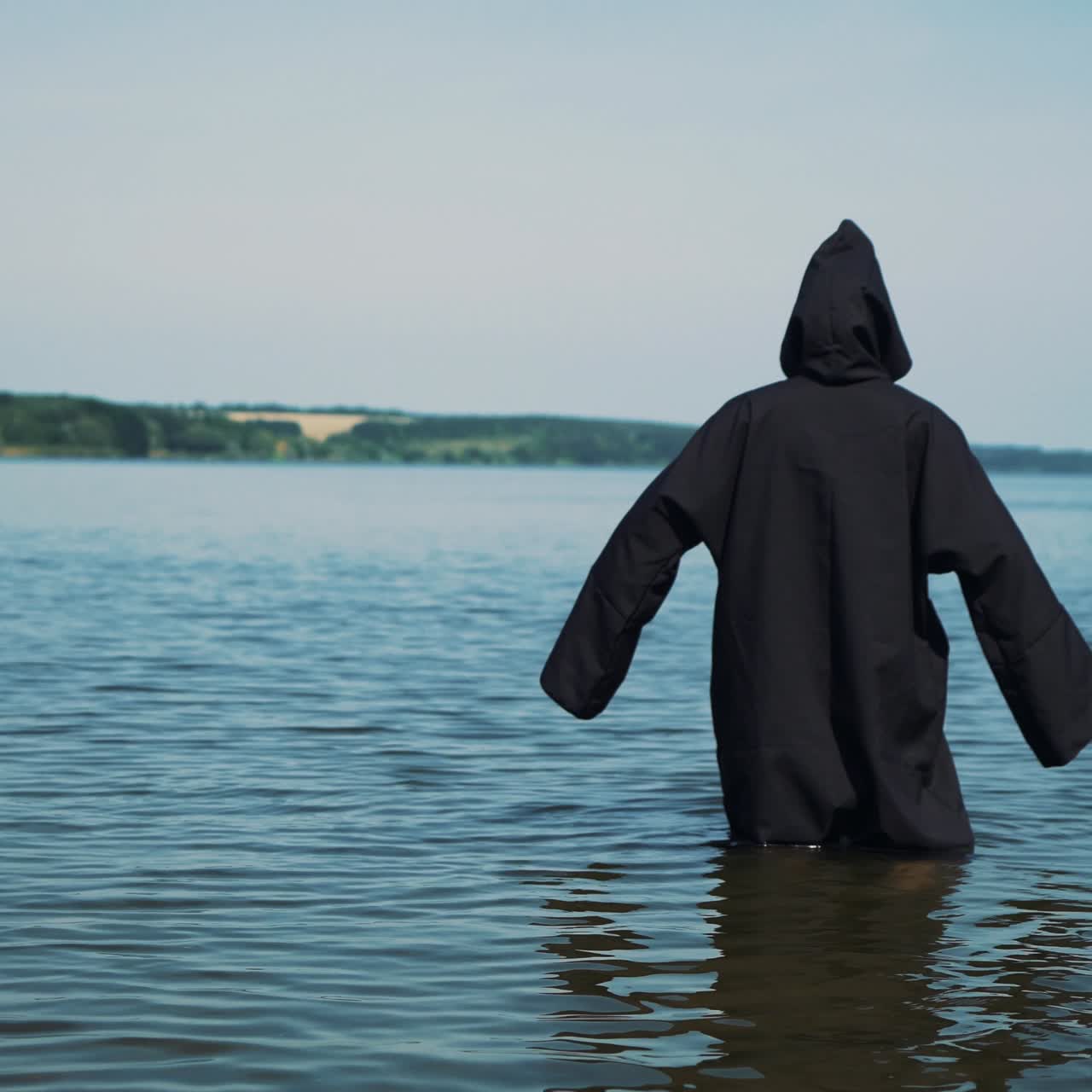 Scary figure in black mantle in the river. Mysticism of Halloween. Halloween costume.