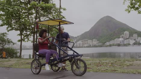 people next to a quadricycle pedal car by a lake with a mountain in the background