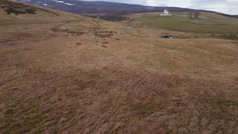 Immersive-drone-shot-starts-with-a-captivating-view-of-a-person-and-a-car,-then-gracefully-pans-over-a-picturesque-brown-field,-leading-to-a-charming-white-church-in-the-serene-background