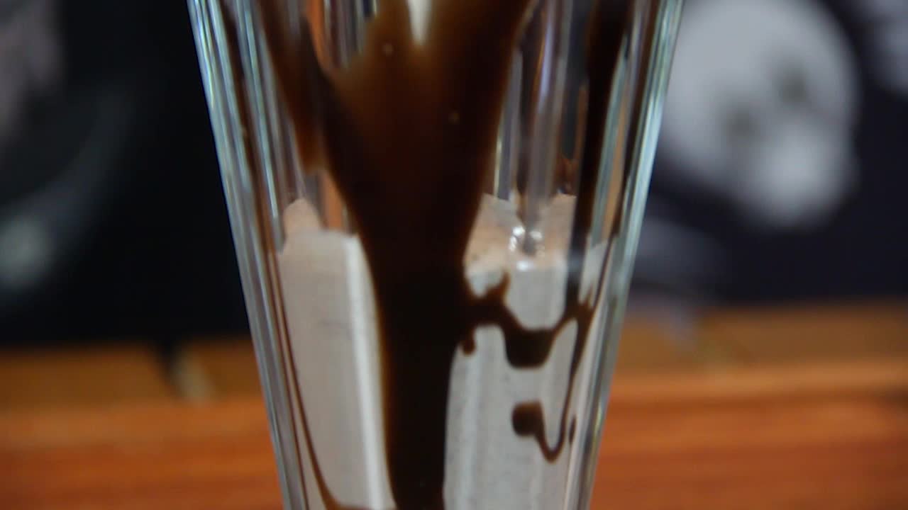 Versamento di milkshake al cioccolato e biscotti in un bicchiere con guarnizioni, al rallentatore e con movimento della telecamera.