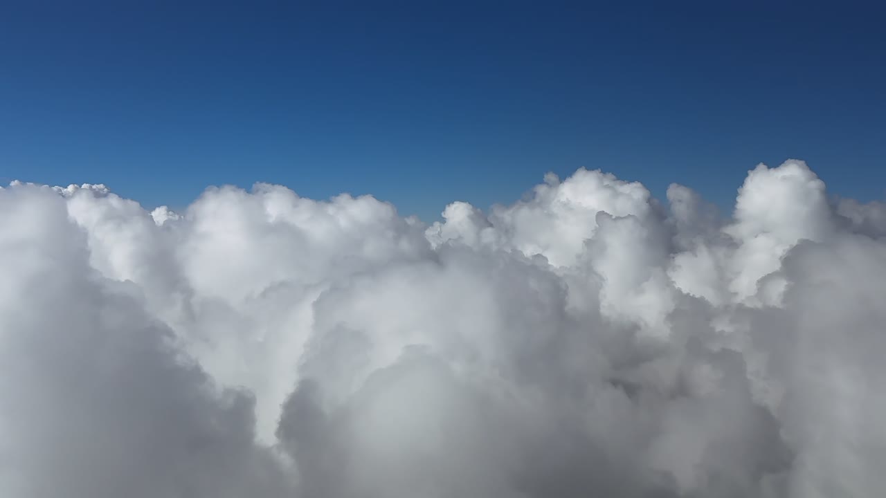 A pilot’s perspective from a jet cokpit while flying art supersonic speed above an endless layer of cottony clouds, doing a left turn, under a deep blue sky