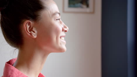 happy biracial teenage girl looking out of window at home smiling, copy space, slow motion