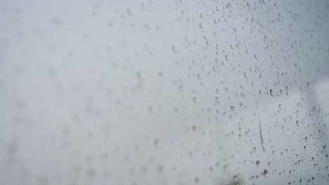 a slow-motion narrow view of heavy raindrops is seen through a window glass