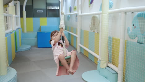 a 4-year-old girl playing on a rope swing inside the playroom - slow motion