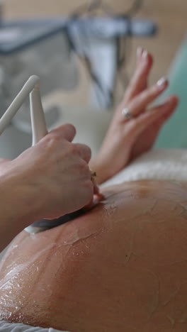expecting woman lies on the obstetrician's couch. female hand moving the sensor by gelled abdomen. close up. vertical video