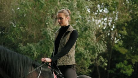 female equestrian climbs on horseback with help of stirrup and strokes a beautiful brown horse