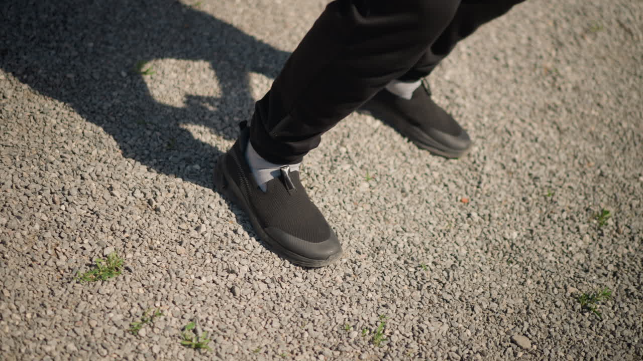 Zapatillas de deporte que se deslizan sobre la grava en una danza rítmica, bailarín urbano dinámico que ejecuta pasos rápidos al aire libre, enérgico bailarín callejero que muestra un juego de pies ágil con sombras texturizadas y calzado informal