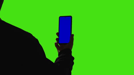 un hombre con un teléfono móvil de pantalla azul de pie contra un fondo de pantalla verde