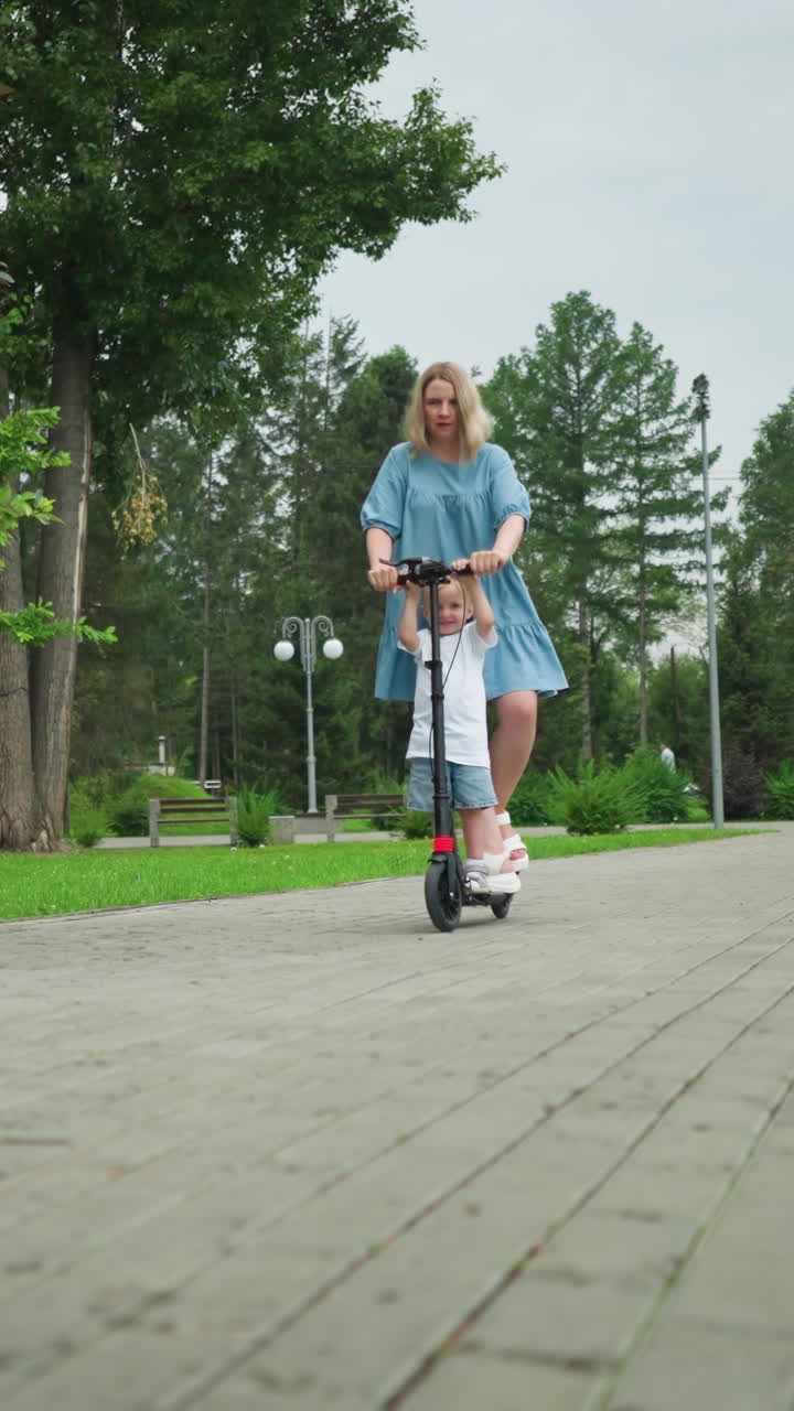 A mother and son riding a scooter down a smooth, interlocked walkway in a peaceful park