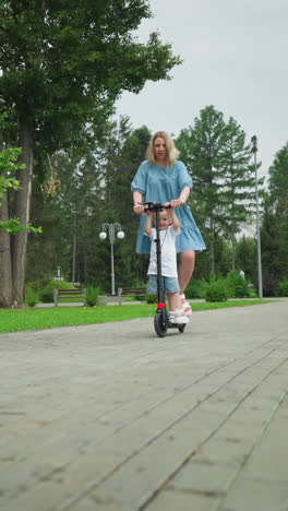 a mother and son riding a scooter down a smooth, interlocked walkway in a peaceful park