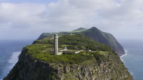 pull back drone footage of a lighthouse revealing dramatic cliffs and the atlantic ocean and the são jorge island shape, in the azores, portugal