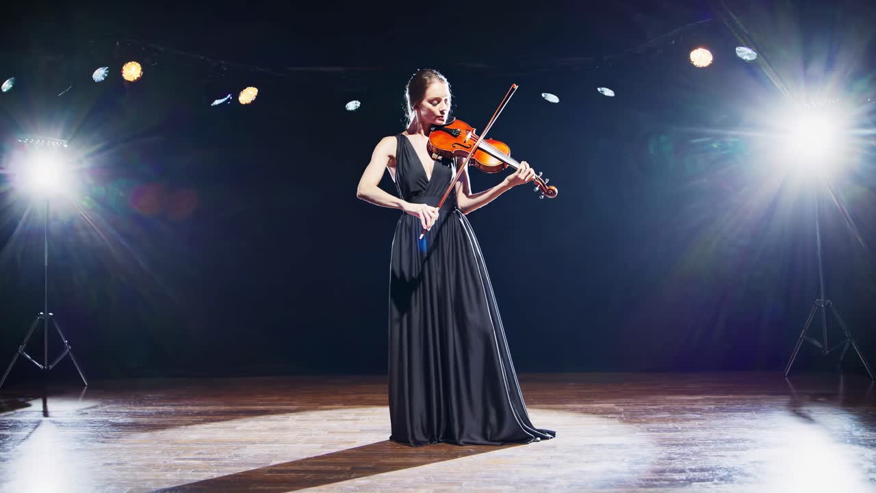 A dramatic video still of a violinist on stage, captured from a low angle