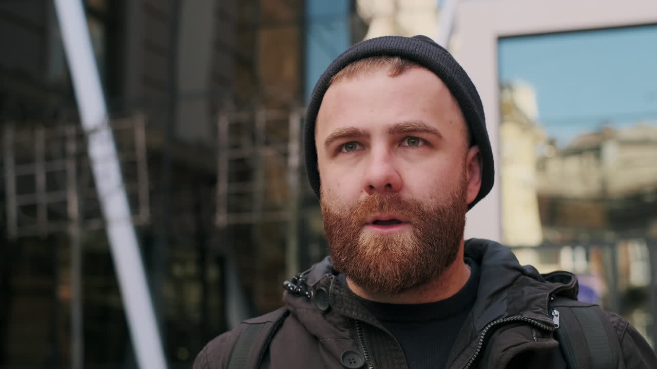 A man with a beard and beanie on a city street