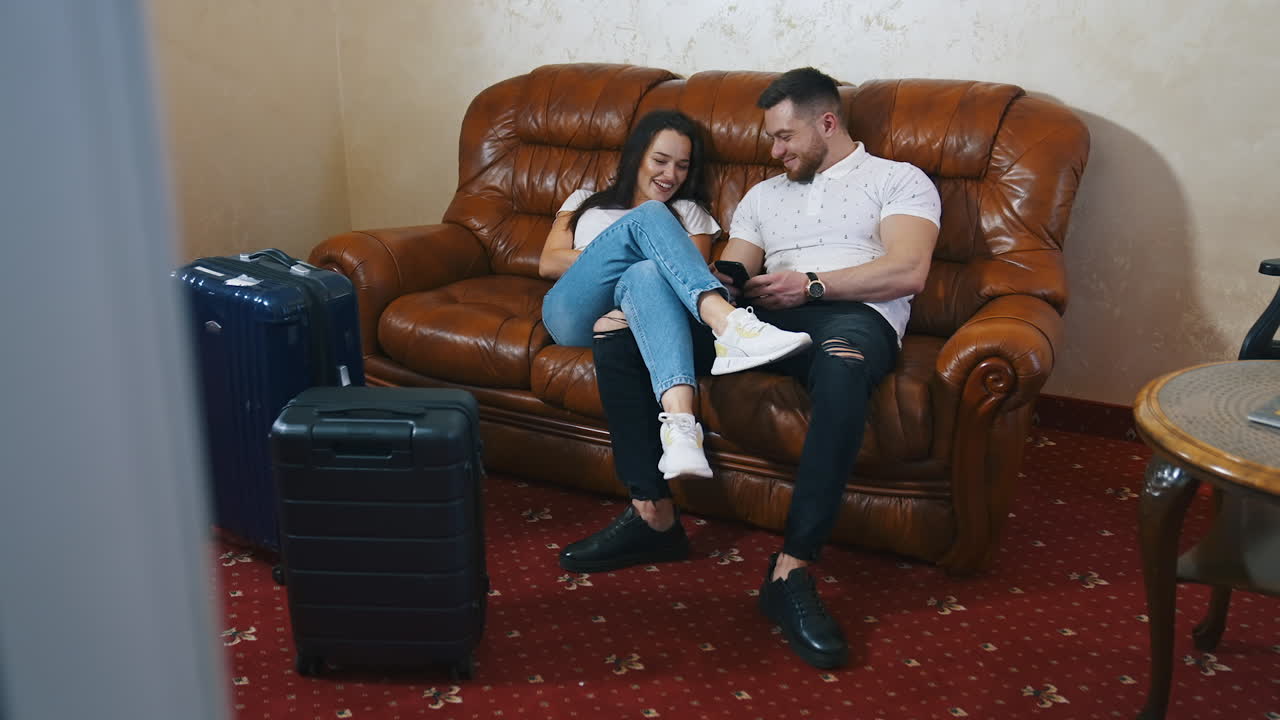 Couple on couch near packed suitcases. Young man and woman resting on a sofa after a long journey in a hotel. Happy couple in love waiting for the departure.