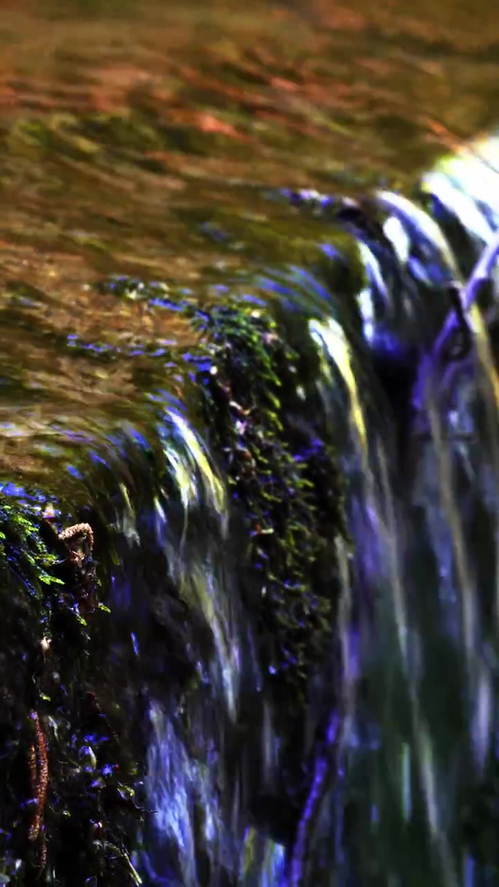Vertical close up of a small waterfall flowing over moss covered rocks along the Rio Gelana river in Bedonia, Parma, Italy.