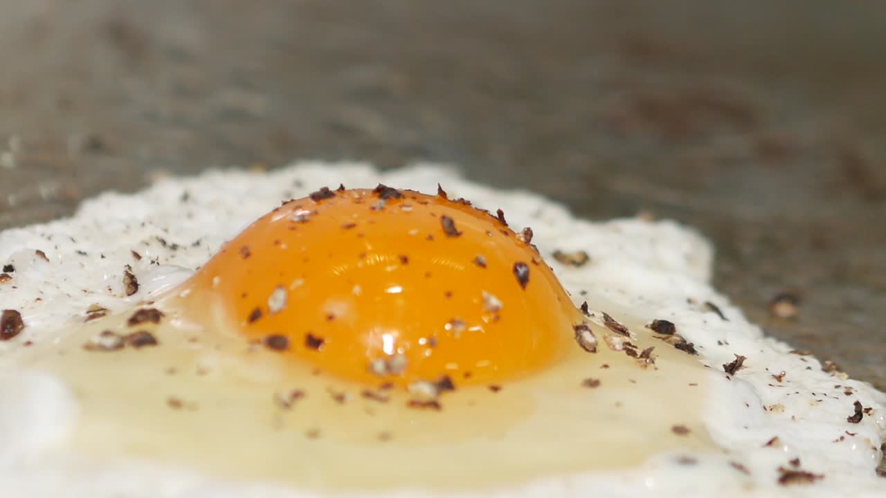 Primo piano macro di un uovo all'occhio di bue che viene condito con pepe mentre è ancora sulla griglia