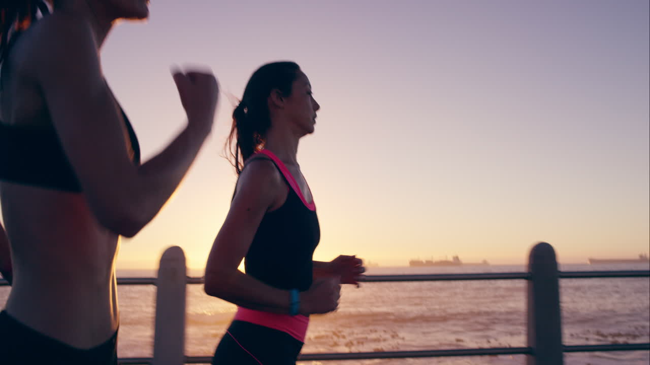 Two athletic woman running outdoors slow motion on promenade at sunset near ocean enjoying evening run