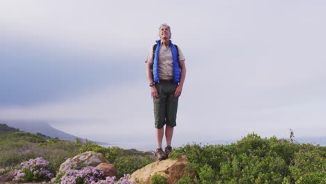 Älterer-Wanderer,-Der-Mit-Weit-Geöffneten-Armen-Auf-Einem-Felsen-Steht,-Während-Er-In-Den-Bergen-Wandert