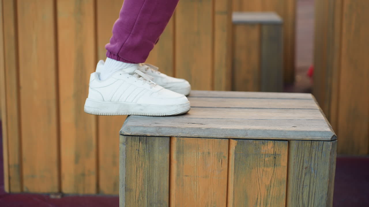 Side view muscular legs in athletic shoes jumping onto wooden plyo box on gym floor against paneled wall showcasing explosive leg power and lower body strength with visible calf contraction