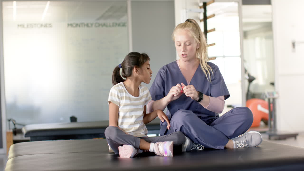 Physical therapist in scrubs helping young girl with cerebral palsy with disability in rehab session