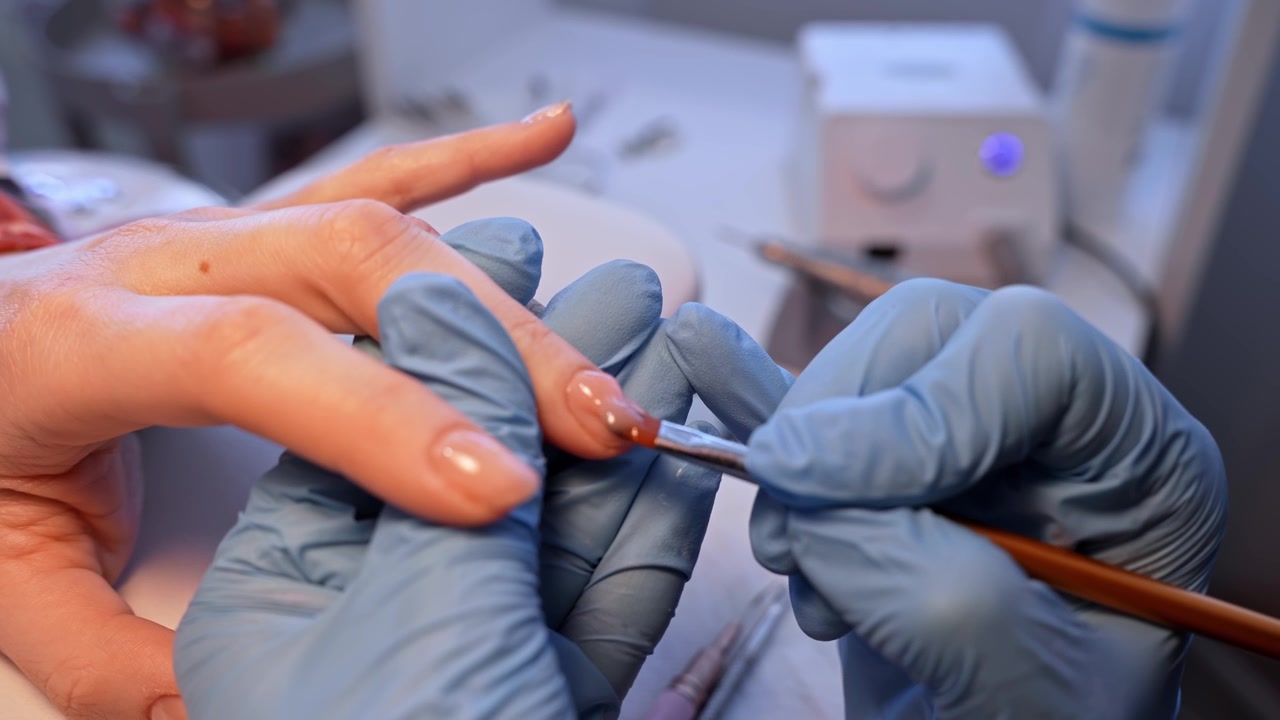 Vista panorámica de un salón donde una manicurista aplica el esmalte final con un pincel, destacando la precisión del acabado, la atención al cliente y el elegante estilo de la manicura profesional.