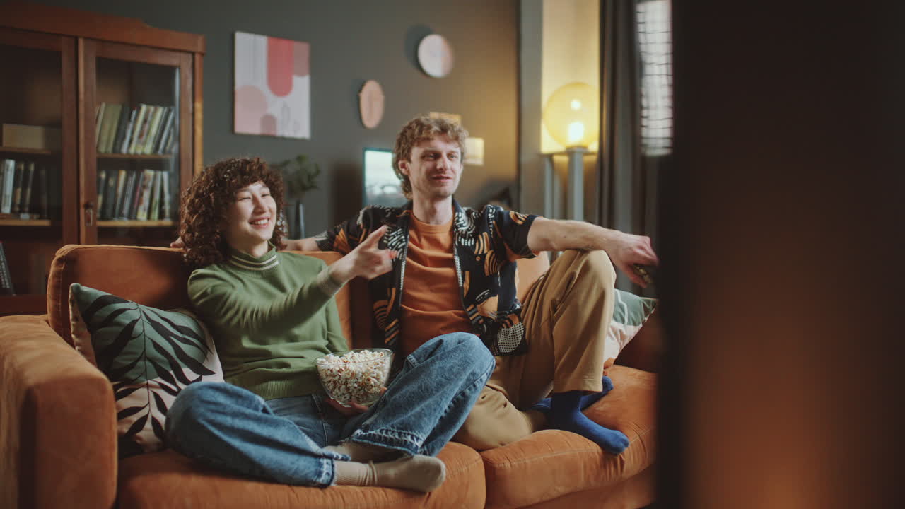 Young Couple Laughing and Enjoying Popcorn as Watching Movie at Home