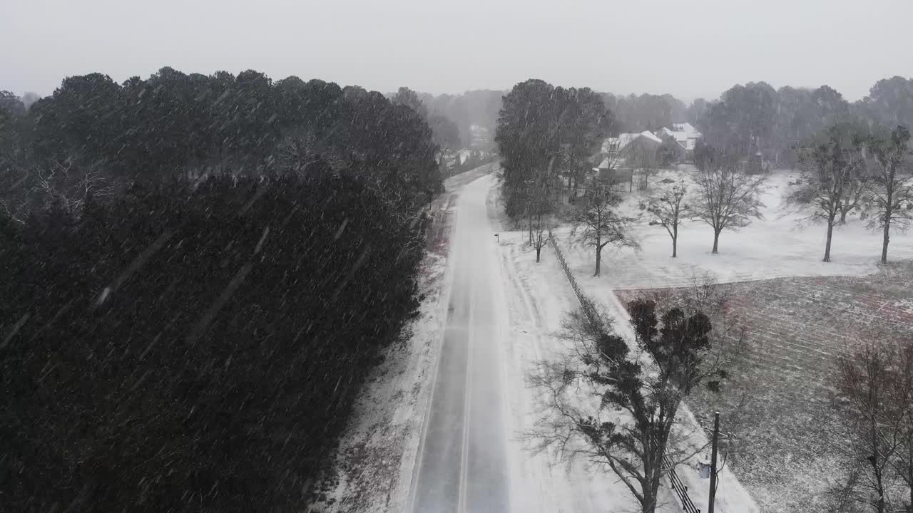 Slow drone video of Snow falling in Georgia quickly covering an empty two lane road