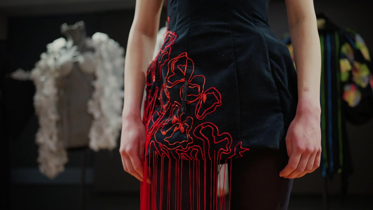 Primo piano di una modella che indossa un abito nero con elementi di filo rosso che si estendono verso l'esterno, creando una tensione lineare attraverso il corpo