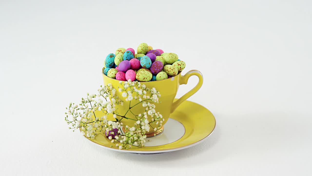 taza llena de huevos de pascua de chocolate pintados y flor blanca