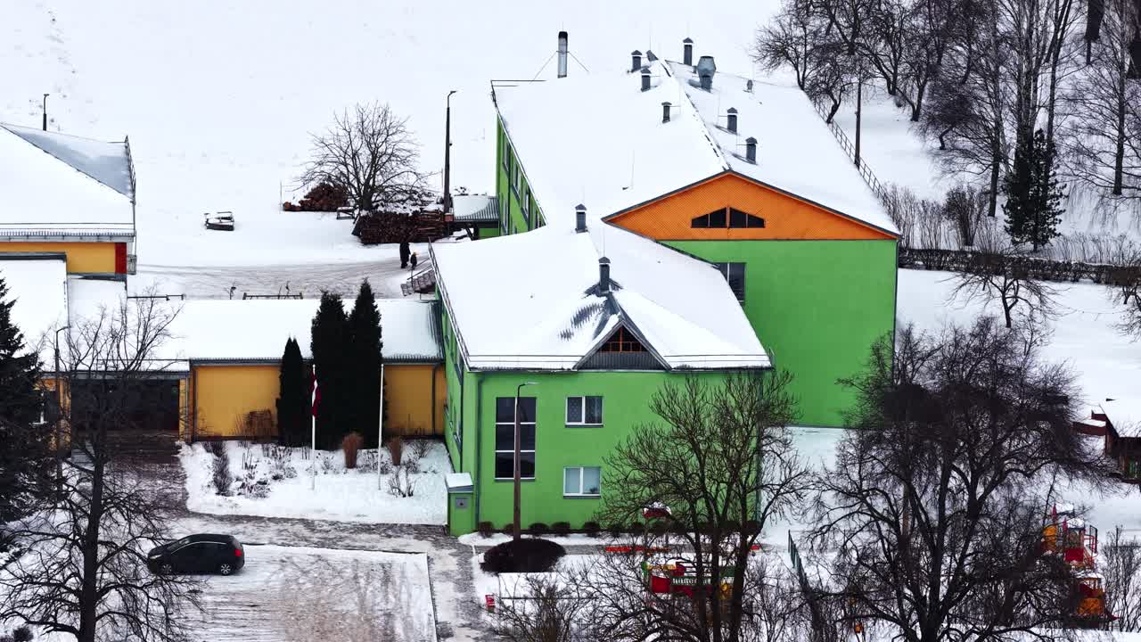 Koulurakennus lumipeitteisellä katolla ja ympäröivällä pihalla kylmänä talvipäivänä.