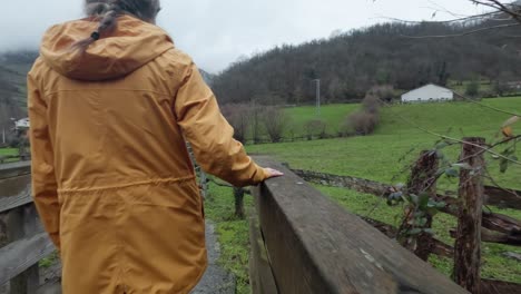 Junge-Dame-Mit-Pferdeschwanz-Und-Regenjacke-überquert-Einen-Fluss-In-Einer-Ländlichen-Umgebung