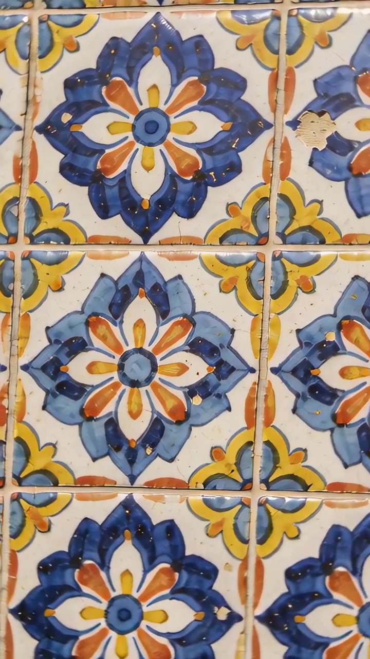 Vertikal video: Panorerende håndholdt kamera over flisepanelinteriør, der viser fuger, afslag og blomstermotiver.