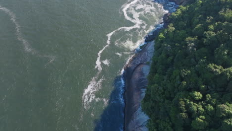 aerial footage flying over the waters of the atlantic ocean washing up against the rocks outside of the city of rio de janeiro