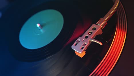 a young man puts a black vinyl record on the player with a close-up on a background of red and blue lights. the needle slides smoothly onto a rotating black vinyl record